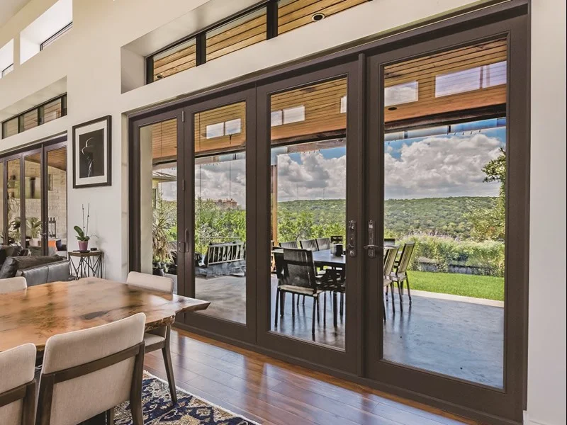 A bronze four panel Neuma folding door opening a dining room to a long view