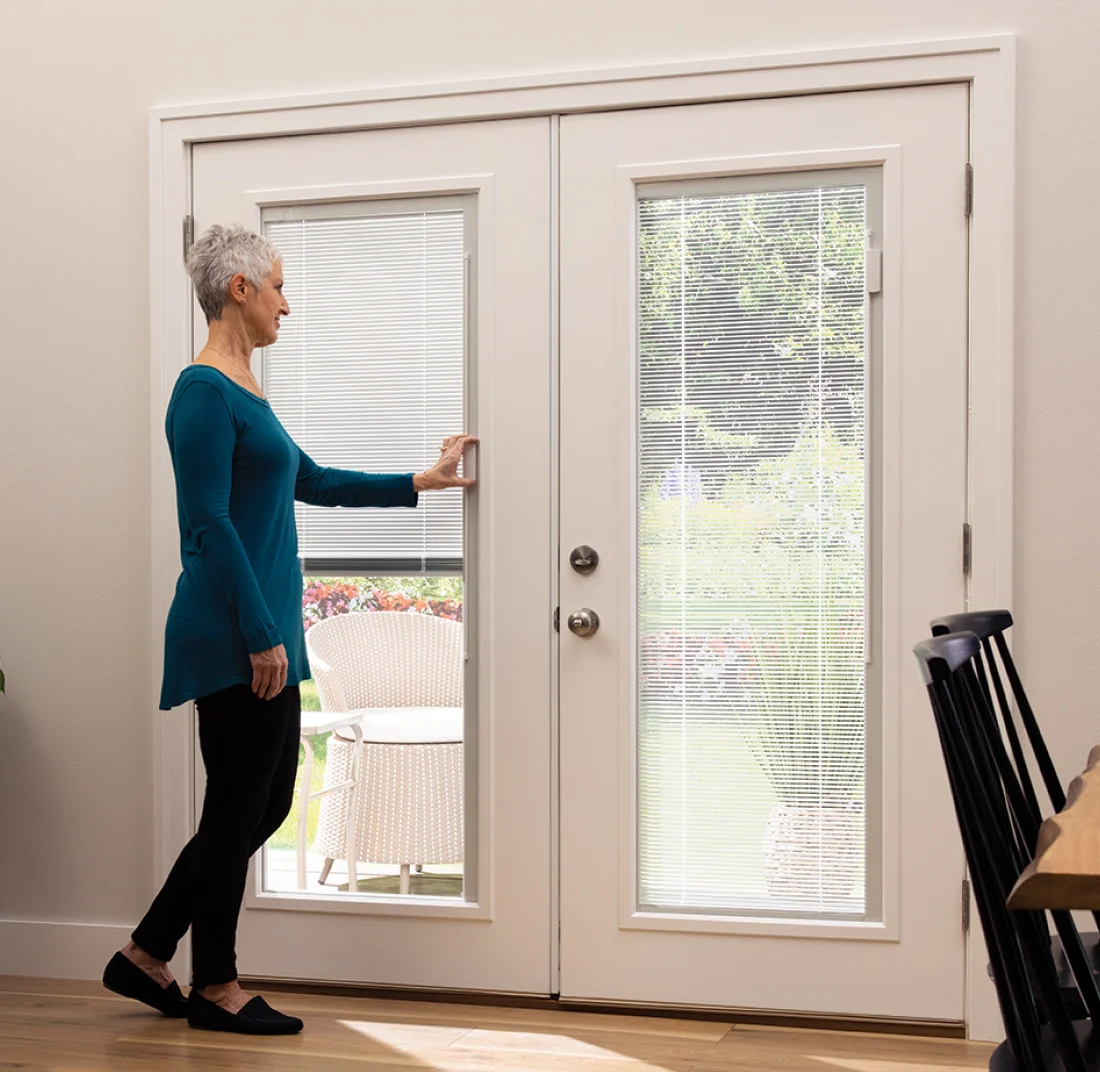 A family room at dusk with a black patio door, the blinds between the glass lowered and the slats nearly closed