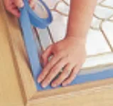 Masking tape applied around a door glass insert before staining