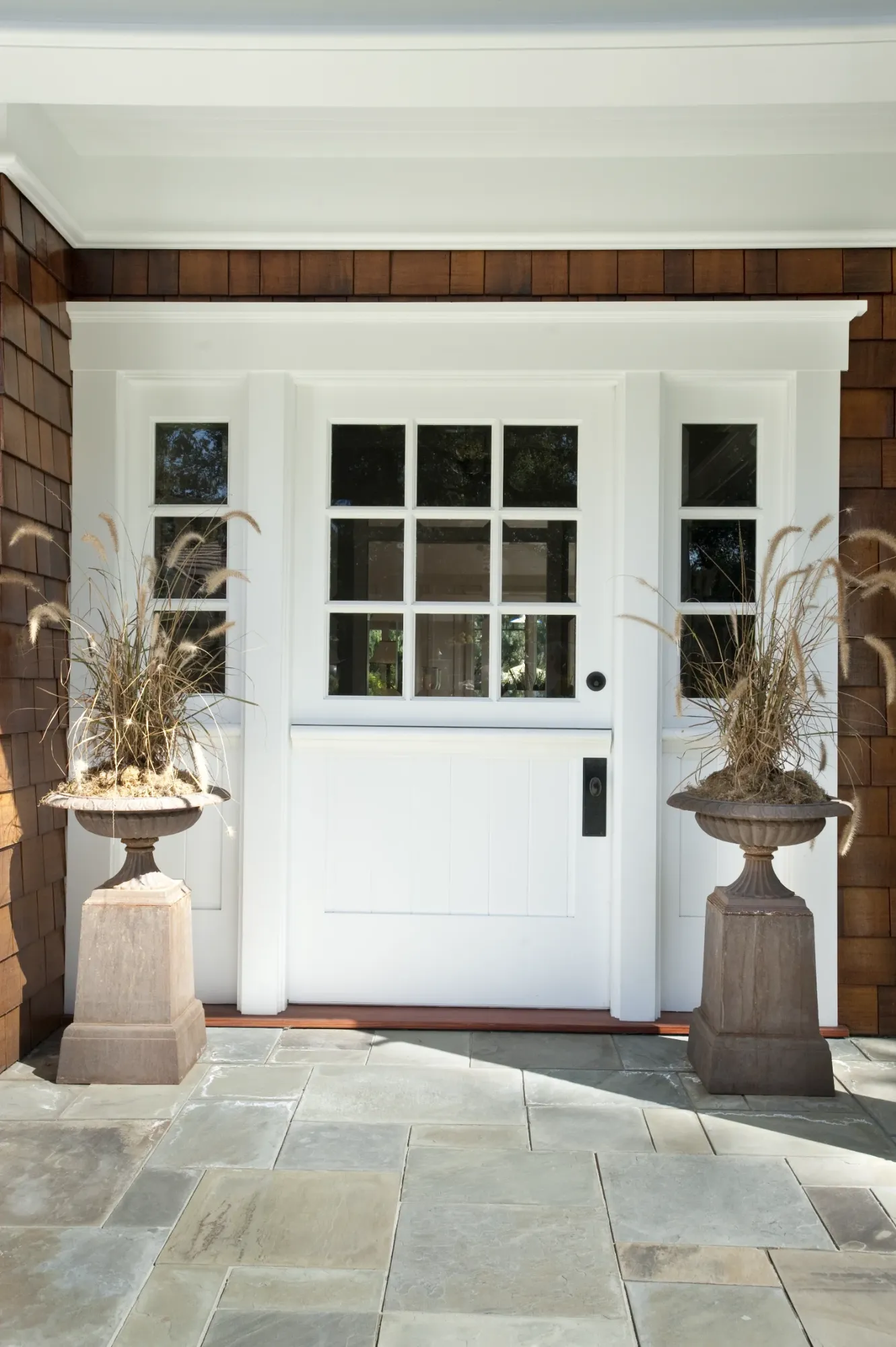 A white nine lite Dutch entry door with matching sidelites on a shingled house