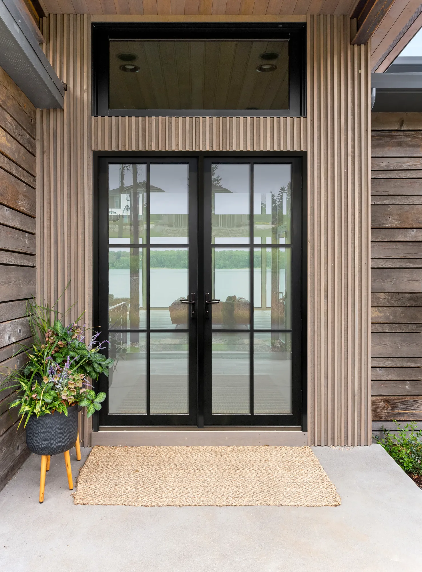 Black French entry doors with divided lites and transom on a wood-clad house