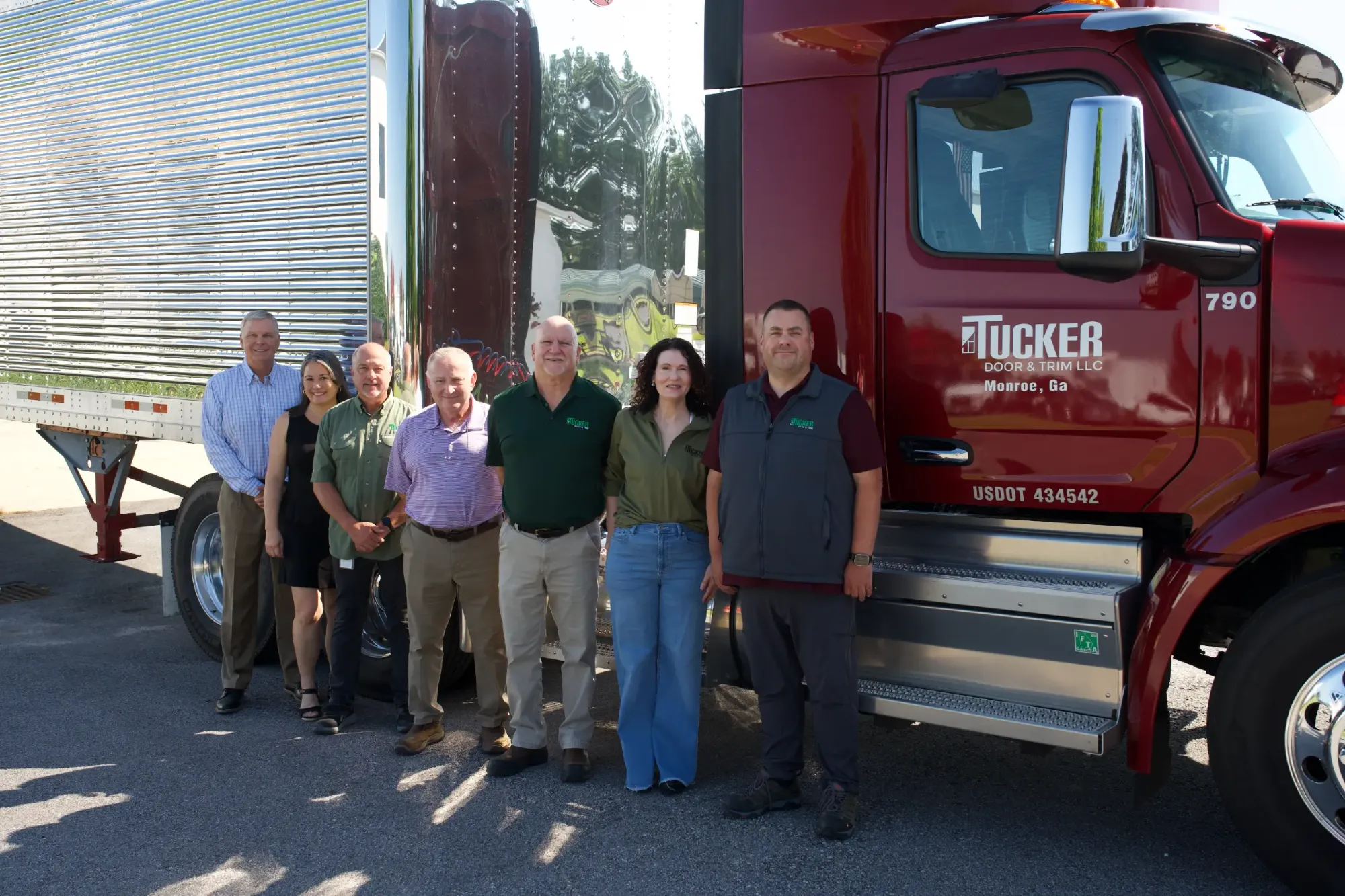 The Tucker Door & Trim leadership group standing together in front of a company tractor