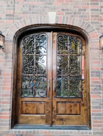 Stained knotty alder arched double entry doors with wrought iron grille work