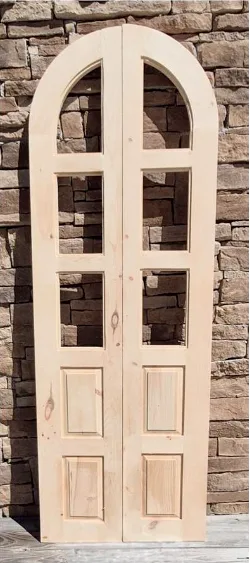 An unfinished arched bifold pair with divided lites standing against a stone wall