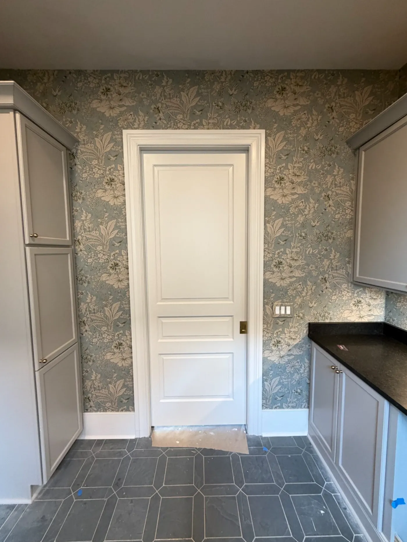 Three panel painted door in a wallpapered pantry