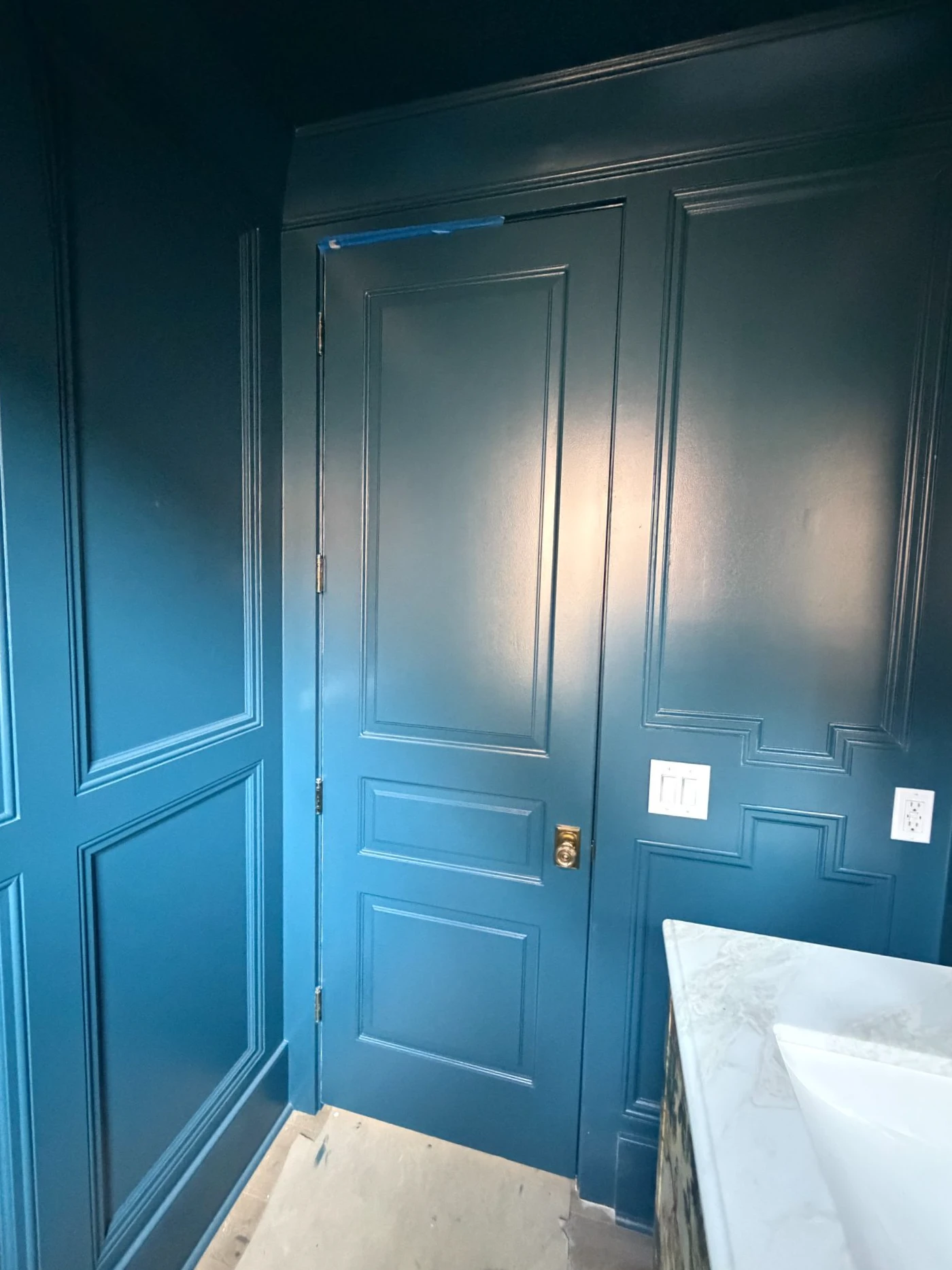 Painted door and applied wall moulding in a dark powder room