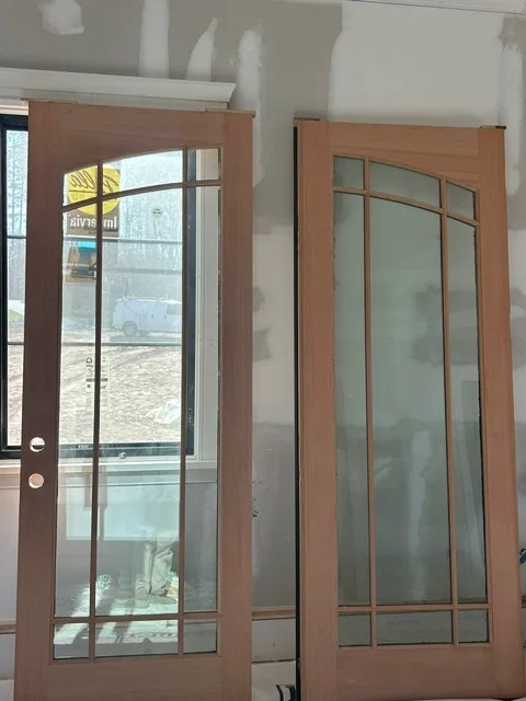 Two mahogany full lite doors with divided lite grids standing in an unfinished room