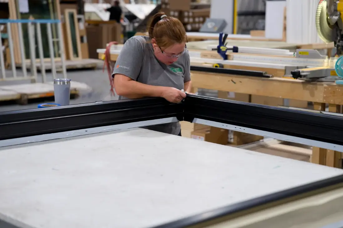 A Tucker employee sealing the corner joint of a black window frame on the assembly bench