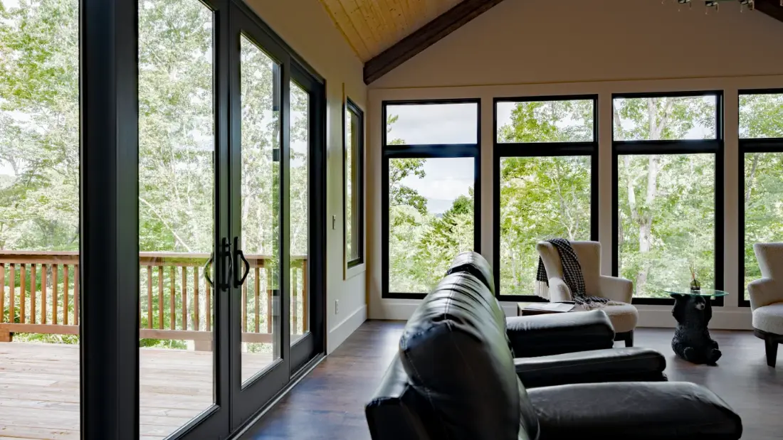 A Neuma patio door and a wall of Tucker 3300 Series vinyl windows opening onto a deck in a vaulted living room