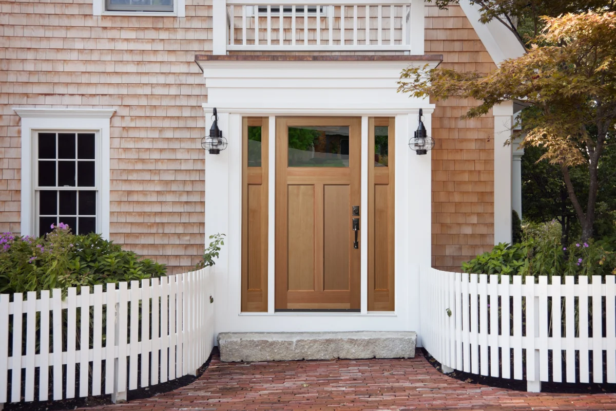 A natural fir Craftsman entry door with a three lite top and matching sidelites, set in a white cedar shingled home
